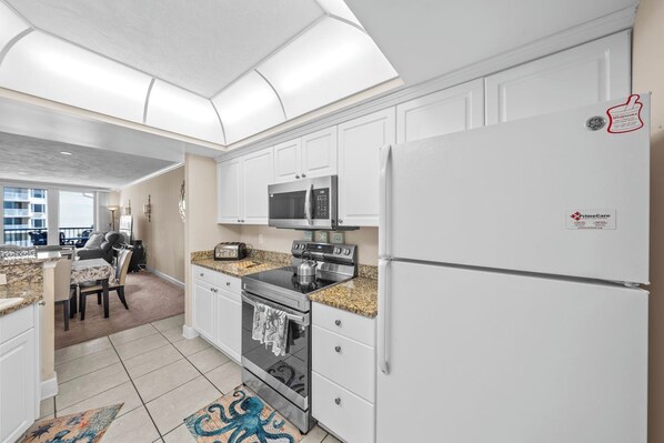 A modern kitchen with white cabinets, a stainless steel refrigerator, a microwave, an oven, and a granite countertop.