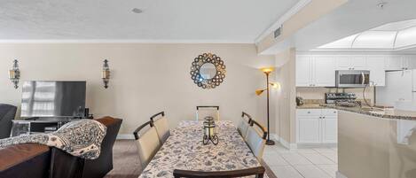Un comedor con una mesa dispuesta para cuatro personas, un televisor y una cocina al fondo.