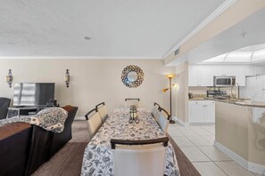 A dining area with a table set for four, a television, and a kitchen in the background.