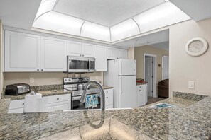 A modern kitchen with white cabinets, a stainless steel microwave, a refrigerator, and a granite countertop.
