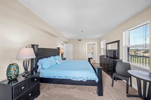 A bedroom with a bed, a dresser, a chair, a table, and a TV. - Towers Grande 301 in Daytona Beach Shores, FL (Daytona Beach Shores)