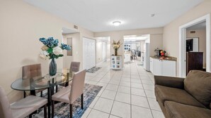 A spacious living area with a glass dining table, beige walls, and a brown sofa.