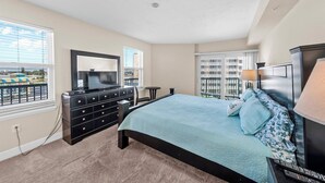 A bedroom with a large bed, a dresser, a TV, and a balcony view.