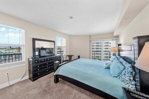 A bedroom with a large bed, a dresser, a TV, and a balcony view.
