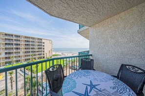 A balcony with a view of the beach, a dining table with chairs, and a building in the background. - Towers Grande 301 in Daytona Beach Shores, FL (Daytona Beach Shores)