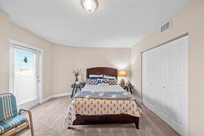 A bedroom with a bed, a chair, a nightstand, a lamp, and a closet.