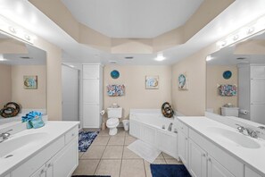A modern bathroom with two sinks, a bathtub, and a toilet. There are decorative wall art pieces and a blue rug on the floor. - Towers Grande 301 in Daytona Beach Shores, FL (Daytona Beach Shores)