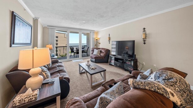 A living room with a sofa, a coffee table, a TV, and a balcony with outdoor furniture.