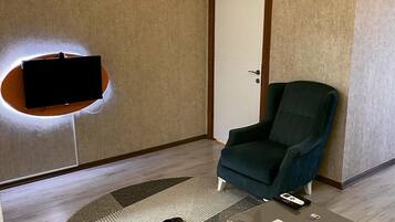 Een moderne woonkamer met een flatscreen televisie aan de muur, een donkere fauteuil, een klein bijzettafeltje en een deur met een airconditioner erboven.