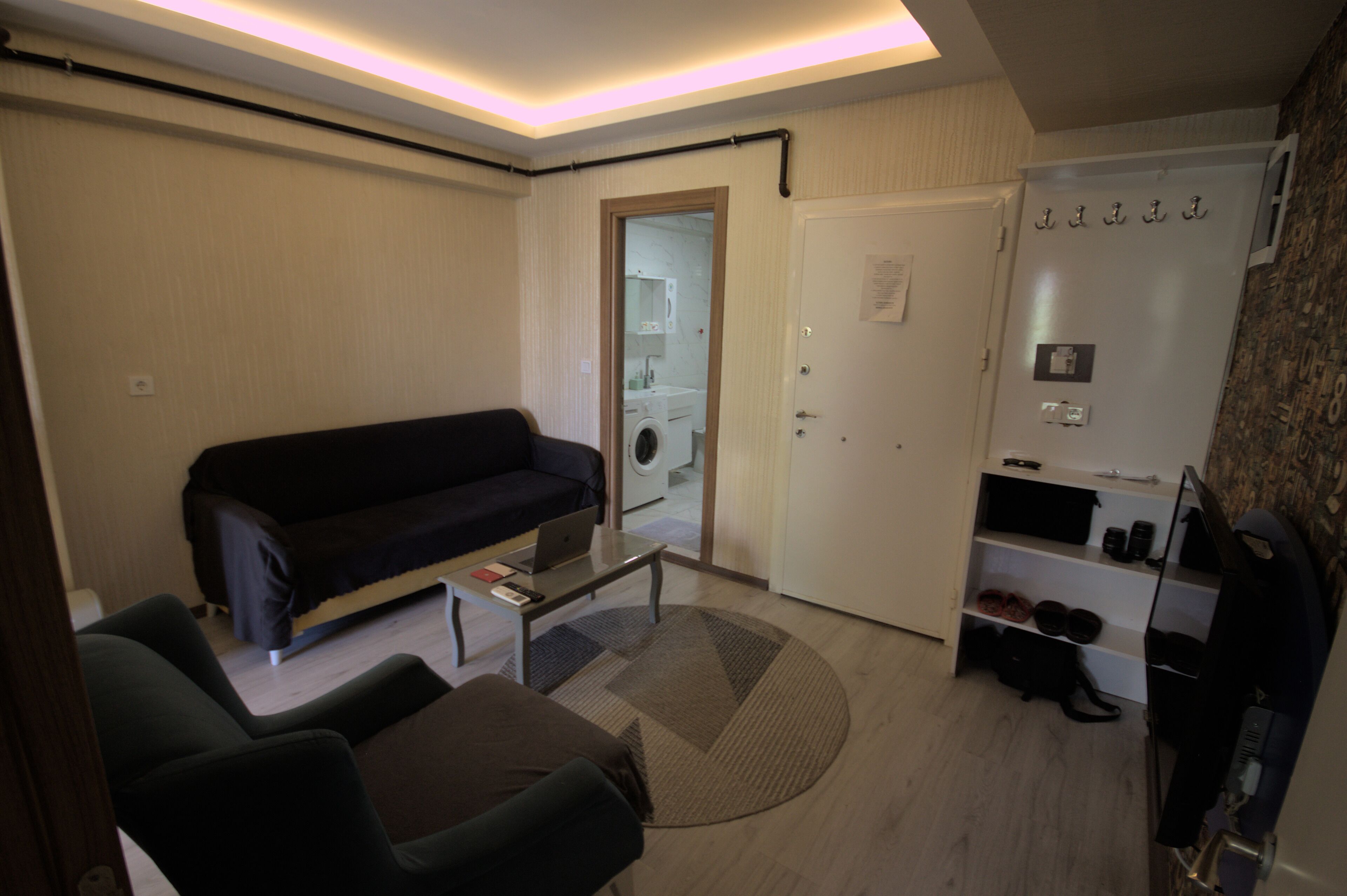 Ein kompakter Wohnbereich mit Sofa, kleinem Tisch, Waschmaschine und Schuhregal.