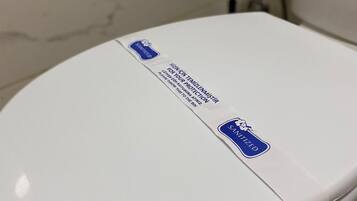Inodoro blanco con tapa y una pegatina azul que indica que está sanitizado.