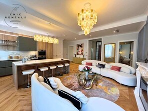 Una sala moderna con un sofá blanco, una mesa de centro redonda y una cocina con barra.