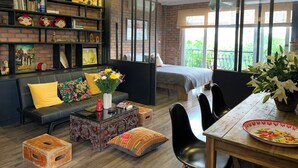 A modern living room with a brick wall, a sofa with colorful cushions, a coffee table, and a dining area with a table and chairs. - Hanoi city center, apartment with all the comforts to visit the city (Hà Nội)
