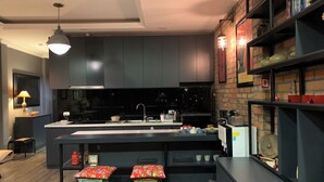 A modern kitchen with dark cabinetry, a central island with stools, and a brick accent wall. - Hanoi city center, apartment with all the comforts to visit the city (Hà Nội)
