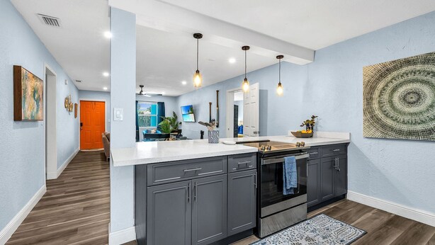 A modern kitchen with dark grey cabinets, a white countertop, and pendant lighting.
