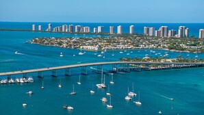 An aerial view of a coastal city with a marina filled with boats, a bridge, and high-rise buildings in the background.