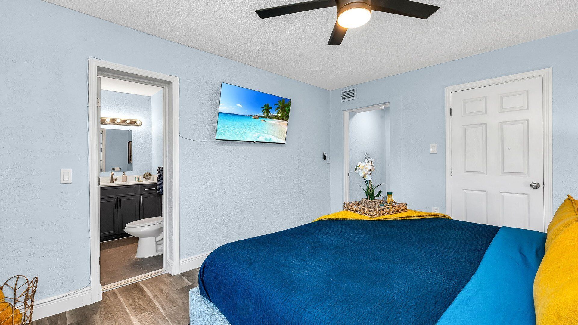 Een slaapkamer met een bed, een plafondventilator, een deur en een zichtbare badkamer door een open deur.