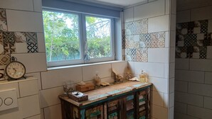 A kitchen with a window, tiled walls, a wooden counter, and a clock.
