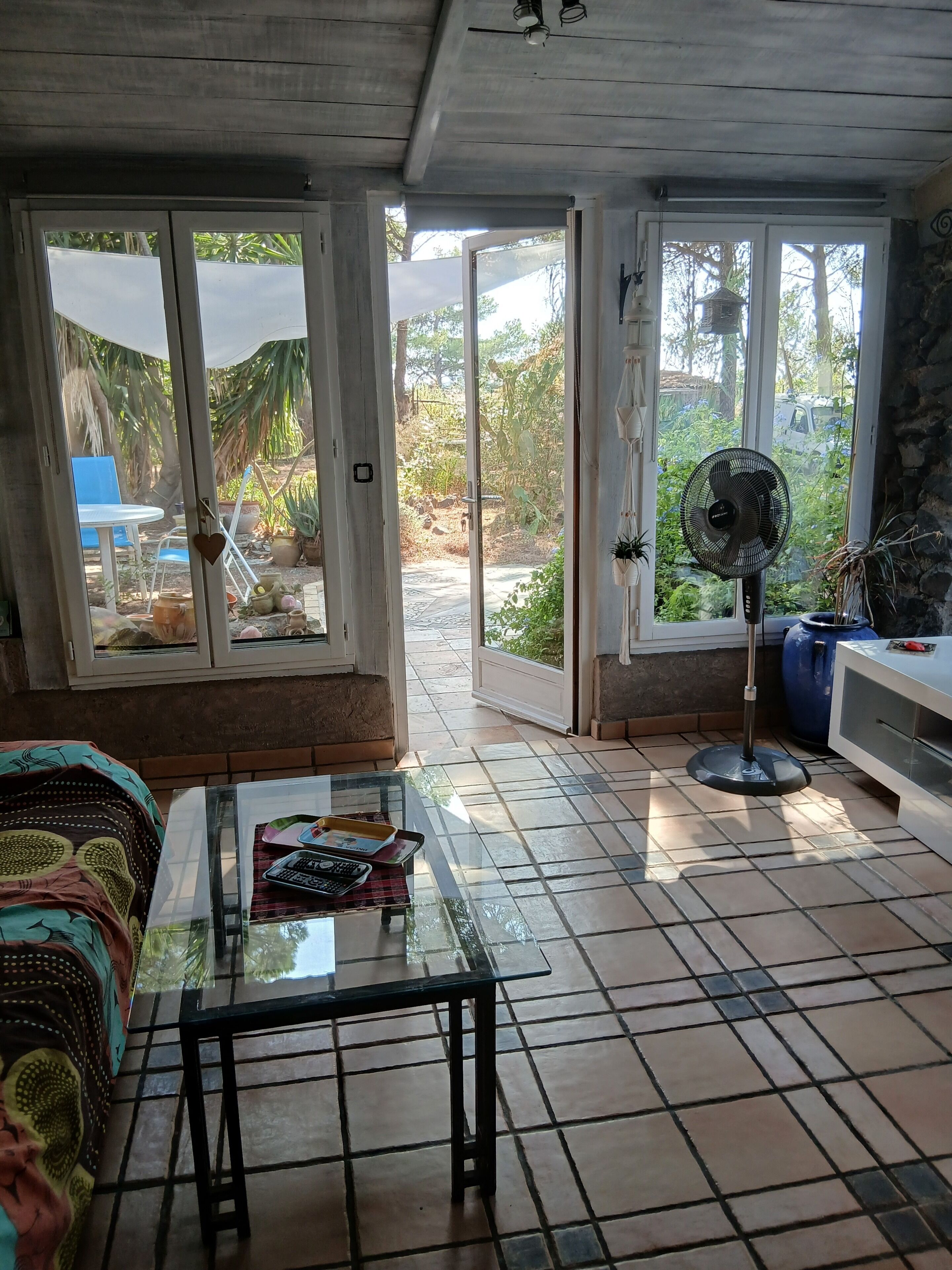 A room with a glass table, a fan, and a view of the outdoors through large glass doors.