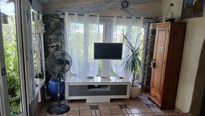 Une pièce équipée d’un téléviseur, d’un ventilateur, d’une plante en pot, d’une armoire en bois et d’un sol carrelé.