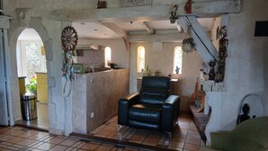 Un salon comprenant un fauteuil en cuir noir, un fauteuil vert et un coin repas avec une table et des chaises.
