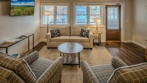 A living room with a beige sofa, two armchairs, a coffee table, and a TV mounted on the wall.