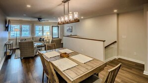 A dining area with a wooden table, chairs, and a chandelier. There is a staircase with a railing leading to an upper level.