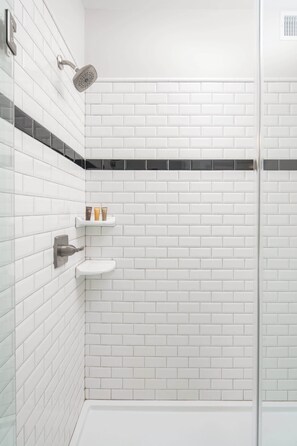 A white-tiled shower area with a handheld showerhead, a small shelf with toiletries, and a white pedestal sink. - Overlook - Downtown, Elevator, Sleeps 6, Parking! (Blowing Rock)