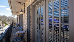 Un balcon avec des fauteuils en osier, une table et une vue sur une rue et des immeubles.