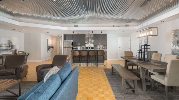 Un salon moderne avec un canapé, des fauteuils, une table à manger et une cuisine en arrière-plan.