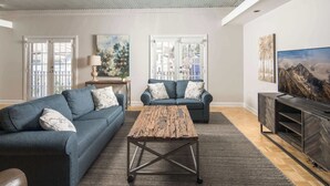 Un salon comprenant deux canapés, une table basse, un meuble pour la télévision et des œuvres d’art accrochées aux murs.