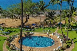 A pool surrounded by palm trees and beach chairs, with a view of the ocean. - Hale Pau Hana #707 Ocean Front, Central AC, Oceanfront Complex (Kihei)