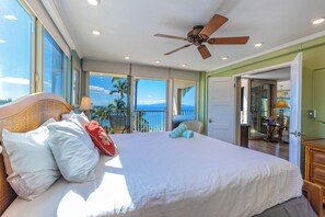 A spacious bedroom with a large bed, a ceiling fan, and a view of the ocean through large windows. - Hale Pau Hana #707 Ocean Front, Central AC, Oceanfront Complex (Kihei)