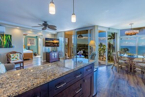 A spacious kitchen with granite countertops, a ceiling fan, and a view of the ocean through large sliding glass doors. - Hale Pau Hana #707 Ocean Front, Central AC, Oceanfront Complex (Kihei)