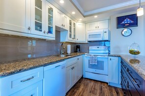 A modern kitchen with white cabinets, granite countertops, a built-in oven, and a microwave. - Hale Pau Hana #707 Ocean Front, Central AC, Oceanfront Complex (Kihei)