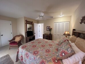 Un dormitorio con cama, una silla, televisor, cómoda, lámpara y armario.
