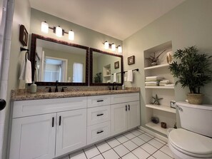 A bathroom with a double vanity, a large mirror, and a toilet. There are towels and toiletries on the counter.