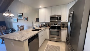 A modern kitchen with white cabinets, stainless steel appliances, a granite countertop, and a patterned rug.