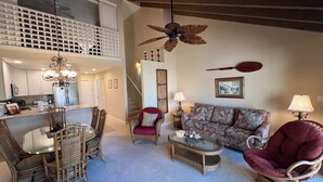 A spacious living area with a high ceiling, a dining table with chairs, a sofa, and a red armchair.