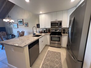 Una cocina moderna con armarios blancos, electrodomésticos de acero inoxidable, encimera de granito y alfombra estampada.