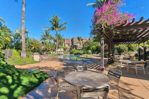 A resort pool area with lounge chairs, a pergola, and palm trees.