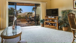 A living room with a glass door leading to an outdoor patio, a television, a bookshelf, and a ceiling fan.