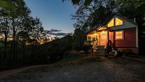 Una cabaña de troncos con un porche, una escalera y vistas del bosque circundante.