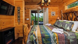 Un dormitorio de cabaña de madera con una cama, un televisor, una chimenea y un ventilador de techo.