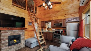 Interior acogedor de una cabaña con chimenea de piedra, paredes de madera, una cocina con electrodomésticos modernos y un espacio de estar confortable.