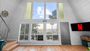 Una habitación amplia con techo alto, ventanas grandes, una escalera y un televisor de pantalla plana que muestra el logotipo de Netflix.