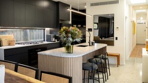 A modern kitchen with dark cabinetry, a granite countertop, and a central island with bar stools. - Seddon Smart Home with Private Pool Getaway (Seddon)