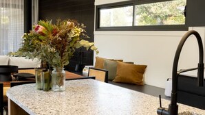A modern kitchen with a granite countertop, black bar stools, a vase with flowers, and a window with a view of trees. - Seddon Smart Home with Private Pool Getaway (Seddon)