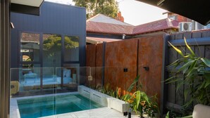 A modern outdoor pool area with glass walls, a wooden fence, and a view of neighboring houses. - Seddon Smart Home with Private Pool Getaway (Seddon)