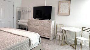Een slaapkamer met een bed, een kaptafel, een televisie en een kleine eethoek met stoelen en een tafel.